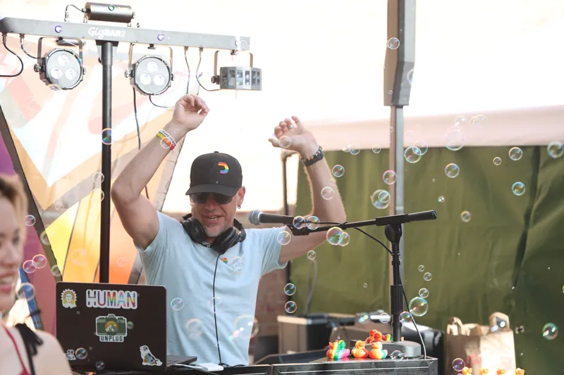 DJ Smilin' Jack with arms raised behind the booth as bubbles fill the air